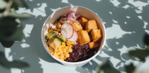 Top view of a vibrant poke bowl with tofu, avocado, and vegetables, surrounded by natural shadows.